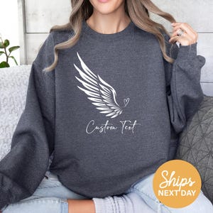 a woman sitting on a couch wearing a grey sweatshirt with a white dove on it