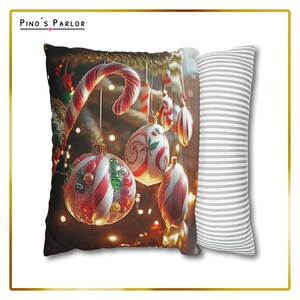 K&ouml;nnte beinhalten: Ein Weihnachts-Wurfkissen mit einem roten und wei&szlig;en Zuckerstangen und roten, wei&szlig;en und gr&uuml;nen Kugeln, die an einem Weihnachtsbaum h&auml;ngen. Das Kissen hat eine wei&szlig;e und graue gestreifte R&uuml;ckseite.