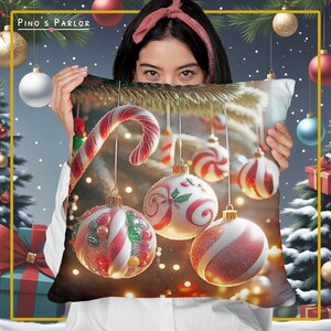 K&ouml;nnte beinhalten: Ein festlicher Weihnachtskissenbezug mit einem roten und wei&szlig;en Zuckerstangen und einer Auswahl an roten, wei&szlig;en und gr&uuml;nen Weihnachtskugeln, die an einem Ast h&auml;ngen. Die Kugeln sind mit einer wei&szlig;en, glitzernden, schnee&auml;hnlichen Substanz bedeckt.