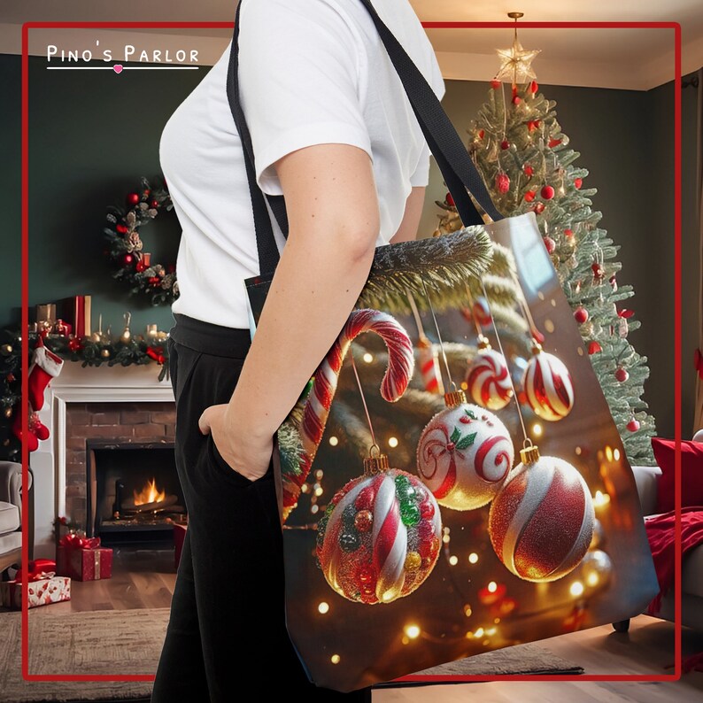 May include: A black tote bag with a Christmas-themed design featuring red and white candy canes and ornaments hanging from a Christmas tree branch. The background is a blurry image of a Christmas tree and a fireplace.