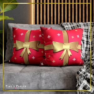 May include: Two red throw pillows with a gold ribbon and bow design. The pillows have a white snowflake pattern on a red background.