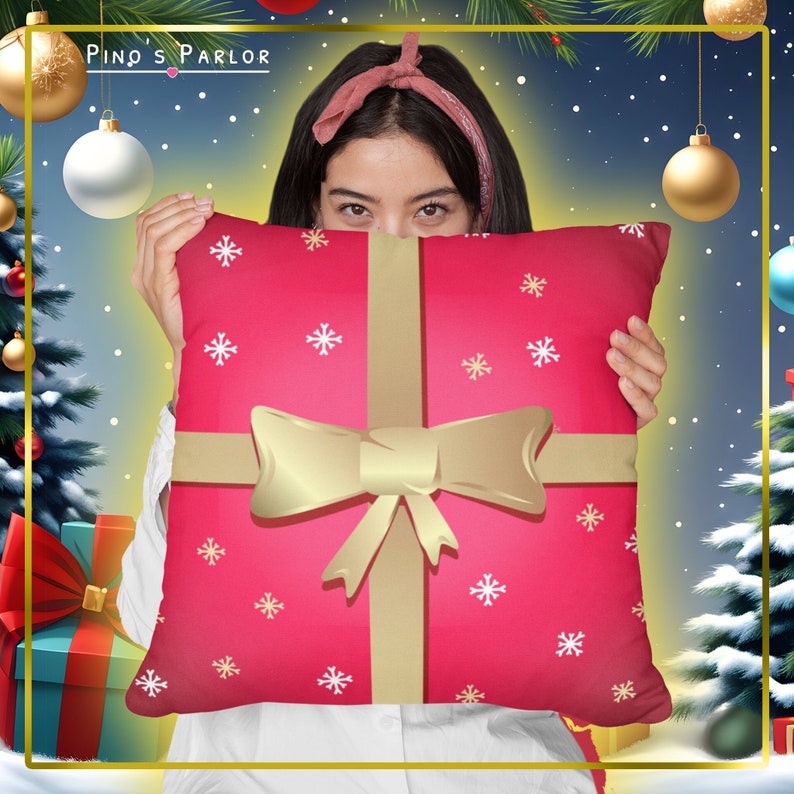 May include: A red and gold throw pillow with a gift box design and white snowflakes. The pillow is being held by a person.