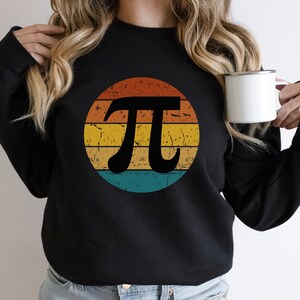 Op de afbeelding: Zwart sweatshirt met een vintage-stijl grafische afbeelding van het wiskundige symbool pi in een cirkel met een regenboogkleurenschema.