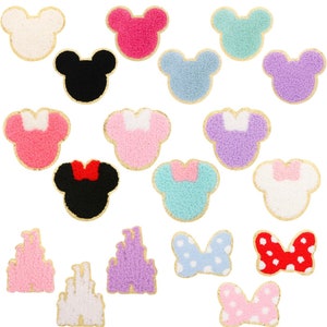 May include: A set of 18 iron-on patches featuring various Disney characters and symbols. The patches are made of fuzzy fabric and have a gold outline. The characters include Mickey Mouse, Minnie Mouse, and the Disney castle. The symbols include bows and hearts.