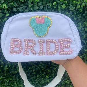 May include: White bridal clutch bag with a pearl-embellished "BRIDE" inscription and a turquoise and pink Minnie Mouse appliqu&eacute;.