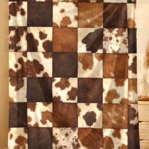 May include: A rectangular throw blanket featuring a chequered pattern of alternating squares. The design consists of solid dark brown squares and squares with a white and brown cowhide print, creating a high-contrast, textured appearance.