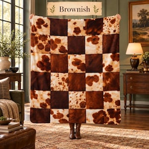 Puede incluir: Una manta rectangular con un patrón de cuadros que alterna cuadrados de color marrón oscuro sólido y cuadrados de color crema con manchas estilo piel de vaca marrón. El texto Brownish aparece en la parte superior central.