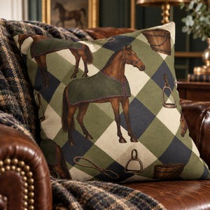 May include: A square throw pillow featuring a repeating pattern of brown horses wearing dark green blankets, wooden buckets, metal stirrups, and rope loops set against a background of large, alternating olive green and navy blue diamond shapes.