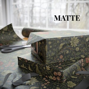 May include: Two gift boxes wrapped in matte black floral patterned paper with red and green accents. The word "MATTE" is printed in black. A pair of scissors and a roll of wrapping paper are visible in the background.
