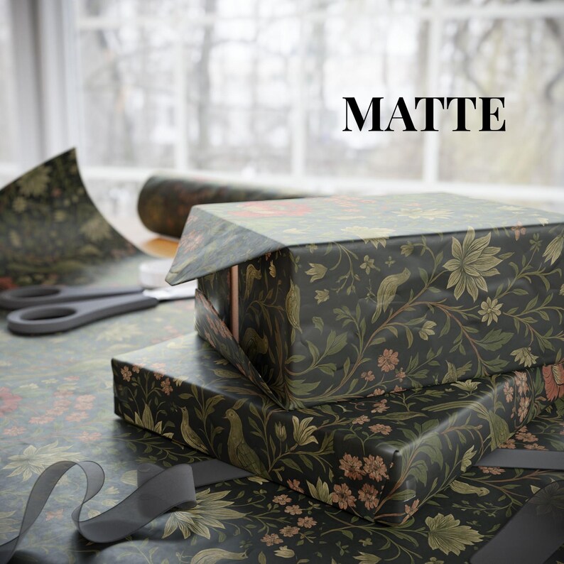 May include: Two gift boxes wrapped in matte black floral patterned paper with red and green accents. The word "MATTE" is printed in black. A pair of scissors and a roll of wrapping paper are visible in the background.