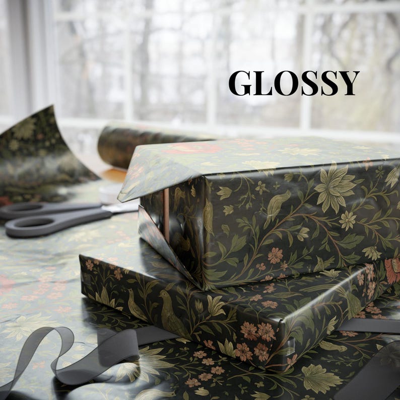 May include: Two gift boxes wrapped in glossy black paper with a floral and bird pattern. The word "GLOSSY" is printed in black. Scissors and a roll of wrapping paper are visible in the background, along with a gray ribbon.