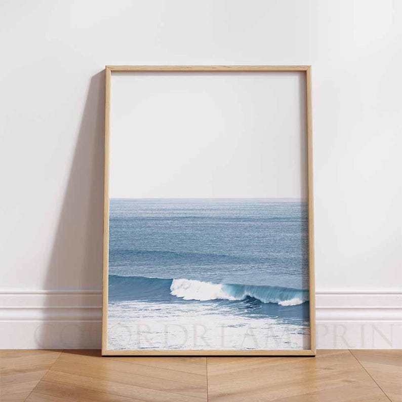 May include: A framed photograph of a blue ocean with a single wave breaking in the foreground. The sky is a light blue and the water is a deep blue.