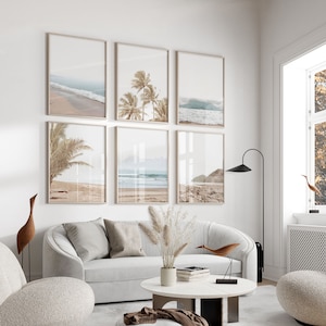 May include: A living room interior with a white couch and a white coffee table. Six framed prints of beach scenes with palm trees and ocean waves hang on the wall. A tall floor lamp and a small wooden bird sculpture are also visible.