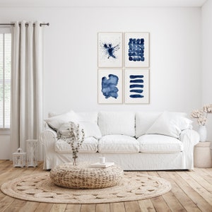 Puede incluir: Cuatro pinturas abstractas de acuarela en tonos azules, dispuestas en una cuadr&iacute;cula en una pared blanca sobre un sof&aacute; blanco. Las pinturas est&aacute;n enmarcadas en un marco simple de madera clara.