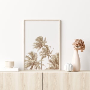 May include: A framed print of a sepia toned photograph of palm trees against a white background. The print is displayed on a light wood shelf with a small wooden bowl and a white decorative object.