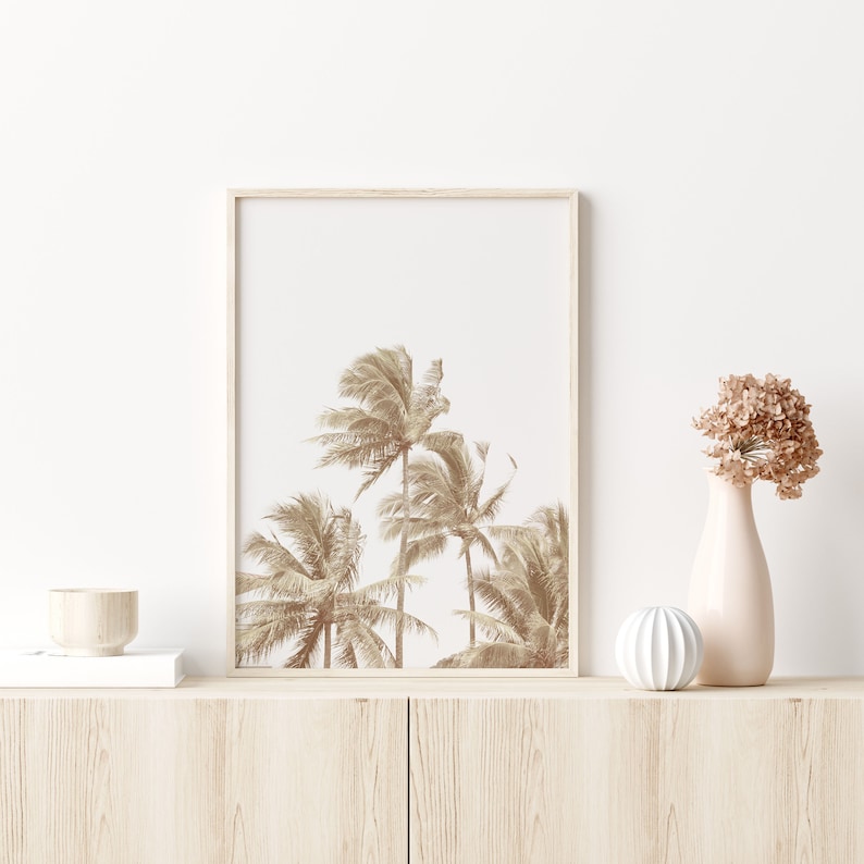 May include: A framed print of a sepia toned photograph of palm trees against a white background. The print is displayed on a light wood shelf with a small wooden bowl and a white decorative object.