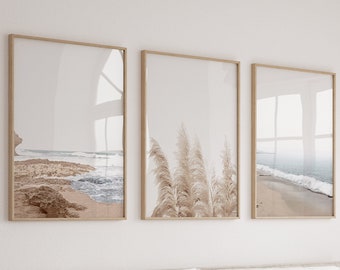 May include: Three framed prints of beach scenes. The leftmost print shows a sandy beach with waves crashing on the shore. The middle print shows a close-up of tall, feathery grasses. The rightmost print shows a sandy beach with waves crashing on the shore.