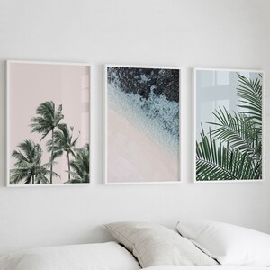 Puede incluir: Tres impresiones enmarcadas con un tema tropical. La impresi&oacute;n de la izquierda presenta un fondo rosa con palmeras. La impresi&oacute;n del centro muestra una playa con agua turquesa y arena blanca. La impresi&oacute;n de la derecha presenta un primer plano de hojas de palmera.