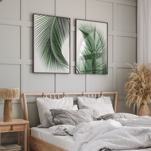 K&ouml;nnte beinhalten: Ein Schlafzimmer mit einem Holzbettgestell und wei&szlig;en Bettw&auml;sche. Zwei gerahmte Drucke von Palmbl&auml;ttern h&auml;ngen an der Wand &uuml;ber dem Bett. Ein Nachttisch aus Holz mit einer Lampe steht neben dem Bett.
