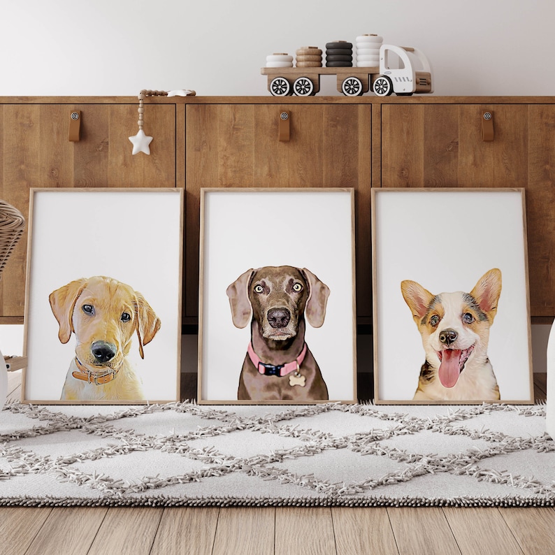 Op de afbeelding: Drie ingelijste prints van hondenportretten. De prints zijn in witte lijsten en tonen een Labrador Retriever, een Weimaraner en een Corgi.