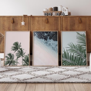 Puede incluir: Tres impresiones enmarcadas con temas tropicales. La impresi&oacute;n de la izquierda presenta palmeras sobre un fondo rosa. La impresi&oacute;n del centro muestra una playa con agua azul y arena blanca. La impresi&oacute;n de la derecha muestra hojas de palmera verdes sobre un fondo azul claro.