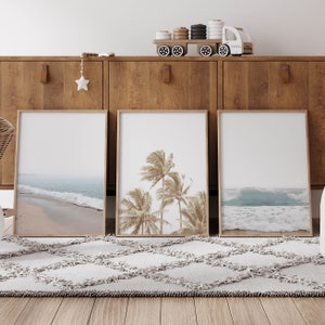 May include: Three framed prints of beach scenes hang on a wooden wall unit. The center print features palm trees, while the prints on either side show ocean waves and sandy beaches.