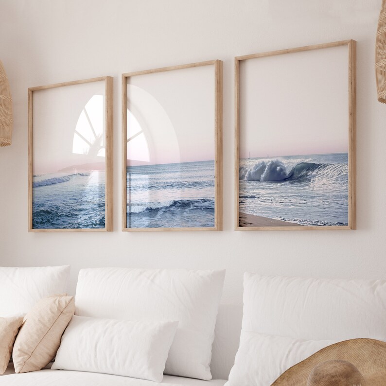 May include: Three framed prints of ocean waves. The prints have light wood frames and feature a serene seascape with blue water and a pink and blue sky. The artwork is displayed on a white wall.