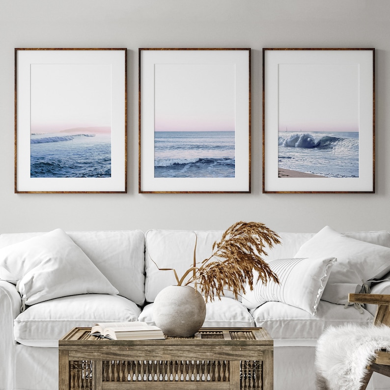 May include: Three framed art prints featuring ocean wave photography. Each print has a brown frame and a white mat. The ocean scenes depict waves in shades of blue and white, with a hint of pink in the sky.