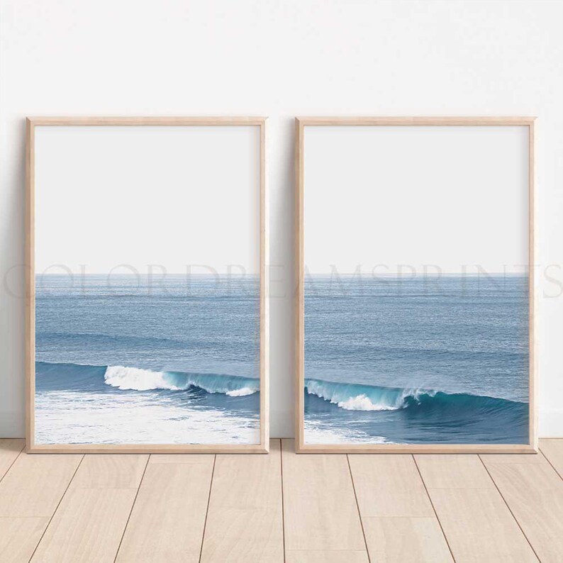 May include: Two framed prints of ocean waves crashing against a blue sea. The prints are in simple wooden frames and are hung on a white wall.