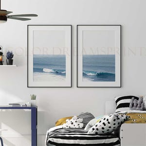 May include: Two black framed prints of ocean waves crashing on a beach. The prints are hung on a white wall above a bed with black and white striped bedding.