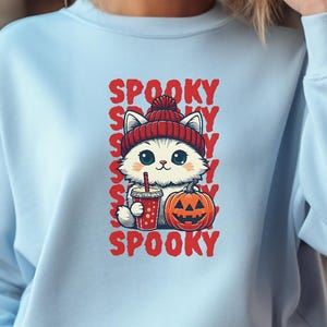 May include: Pale blue sweatshirt featuring a cartoon cat in a red beanie, holding a drink and a carved pumpkin. The word "SPOOKY" is repeated vertically. The top text reads "EXAMPLES OF PROJECT APPLICATIONS" and the bottom text says "NO PHYSICAL PRODUCT WILL BE SEND".