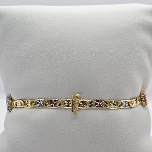 May include: A gold bracelet with a decorative chain link design. The bracelet features a small figure and accents of rose, white, and yellow gold. The bracelet is displayed on a white surface.