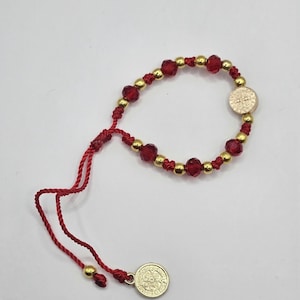 May include: Red and gold beaded bracelet with a Saint Benedict medal charm. The bracelet is adjustable with a sliding knot.