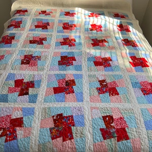 K&ouml;nnte beinhalten: Eine wei&szlig;e Steppdecke mit Patchwork-Muster aus roten, rosa, blauen und gr&uuml;nen Quadraten. Die Steppdecke ist aus verschiedenen Stoffen gefertigt, darunter Blumenmuster und Streifen.