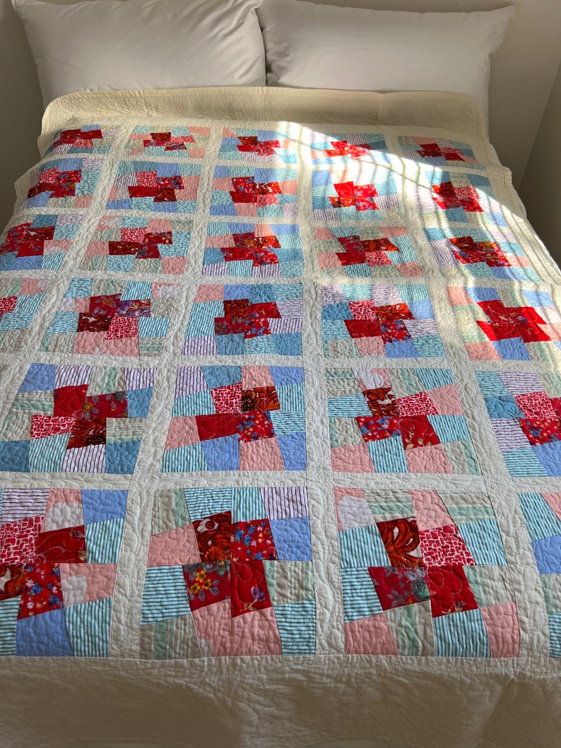 K&ouml;nnte beinhalten: Eine wei&szlig;e Steppdecke mit Patchwork-Muster aus roten, rosa, blauen und gr&uuml;nen Quadraten. Die Steppdecke ist aus verschiedenen Stoffen gefertigt, darunter Blumenmuster und Streifen.