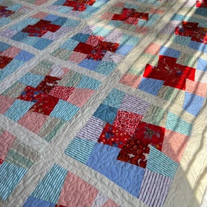 K&ouml;nnte beinhalten: Eine Patchwork-Decke mit einer Vielzahl von roten, blauen, rosa und gr&uuml;nen Stoffen. Die Decke besteht aus Quadraten und Rechtecken, und die Stoffmuster umfassen Streifen, Blumenmuster und einfarbige Stoffe.