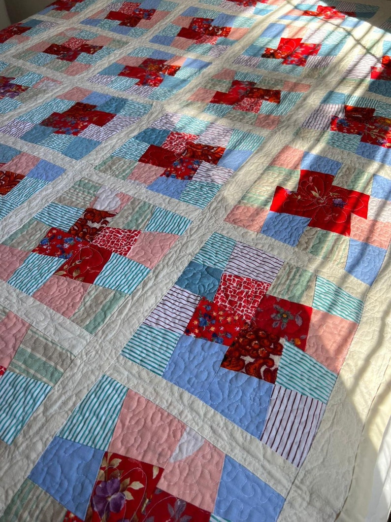 K&ouml;nnte beinhalten: Eine Patchwork-Decke mit einer Vielzahl von roten, blauen, rosa und gr&uuml;nen Stoffen. Die Decke besteht aus Quadraten und Rechtecken, und die Stoffmuster umfassen Streifen, Blumenmuster und einfarbige Stoffe.