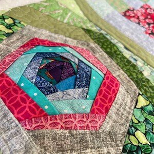 Peut inclure: Gros plan sur un bloc de courtepointe color&eacute; avec un motif de moulin &agrave; vent. Le bloc est compos&eacute; de diff&eacute;rents tissus dans des tons de vert, bleu, rose et blanc. Le centre du moulin &agrave; vent est un tissu violet fonc&eacute;.