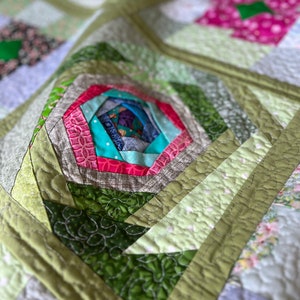 Peut inclure: Une courtepointe en patchwork vert, rose et bleu avec un motif de moulinet au centre. La courtepointe est faite de diff&eacute;rents tissus avec des motifs diff&eacute;rents.