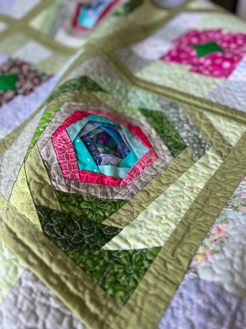 Peut inclure: Une courtepointe en patchwork vert, rose et bleu avec un motif de moulinet au centre. La courtepointe est faite de diff&eacute;rents tissus avec des motifs diff&eacute;rents.