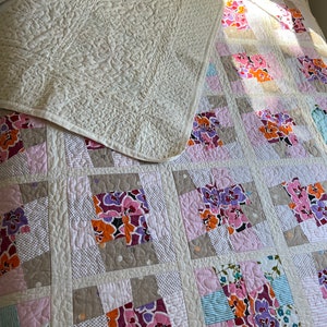 以下が含まれることがあります： 花柄の白いキルト。キルトは異なる生地の正方形で構成されており、それぞれ異なる花柄のデザインが施されています。キルトは半分に折り畳まれ、上半分は下半分に折り畳まれています。