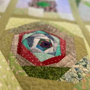 Peut inclure: Gros plan sur une courtepointe verte et blanche avec un motif en spirale au centre. La spirale est faite de diff&eacute;rents tissus, dont du rouge, du vert, du bleu et du blanc. La courtepointe est matelass&eacute;e avec un fil blanc.