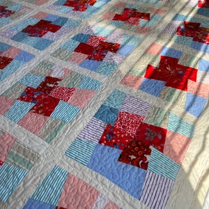 K&ouml;nnte beinhalten: Eine Patchwork-Decke mit einer Vielzahl von roten, rosa, blauen und gr&uuml;nen Stoffen. Die Decke besteht aus Quadraten und Rechtecken, und die Stoffmuster umfassen Streifen, Blumenmuster und einfarbige Stoffe.