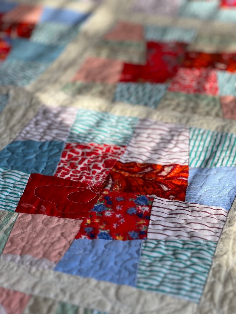 K&ouml;nnte beinhalten: Eine Patchwork-Decke mit verschiedenen roten, blauen und wei&szlig;en Stoffen. Die Decke besteht aus Quadraten und Rechtecken, die N&auml;hte sind sichtbar. Die Decke ist mit einem einfachen Stich gesteppt.