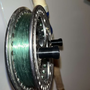 May include: A silver fishing reel with a green line wound around it. The reel has two black knobs on the side.