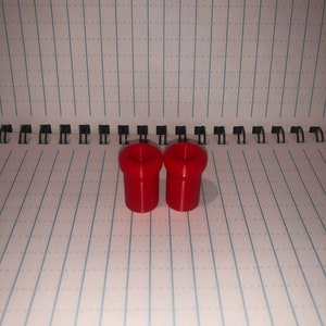 Peut inclure: Deux bouchons de bouteille en plastique rouge. Les bouchons sont cylindriques avec un sommet l&eacute;g&egrave;rement &eacute;vas&eacute;.