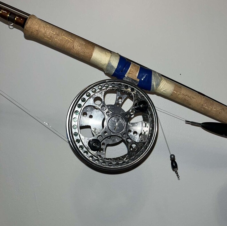 Peut inclure: Un moulinet de p&ecirc;che argent&eacute; avec une poign&eacute;e noire et une canne &agrave; p&ecirc;che en li&egrave;ge avec du ruban adh&eacute;sif bleu. La ligne de p&ecirc;che est attach&eacute;e &agrave; un plomb argent&eacute;.