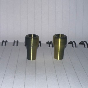 Peut inclure: Deux bouchons en m&eacute;tal de couleur dor&eacute;e avec un dessus l&eacute;g&egrave;rement plus fonc&eacute; et une finition lisse et brillante.