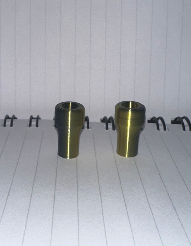 Peut inclure: Deux bouchons en m&eacute;tal de couleur dor&eacute;e avec un dessus l&eacute;g&egrave;rement plus fonc&eacute; et une finition lisse et brillante.