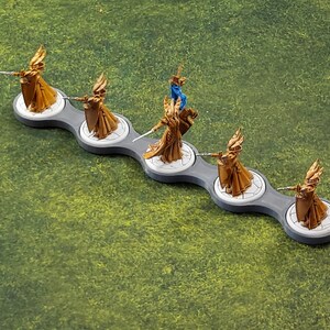 May include: Five gold-painted miniature figures of women wearing flowing robes and holding swords, standing on a grey and white plastic base with a connected design.